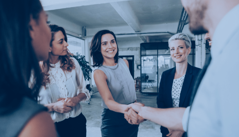 Equipe composta por quatro mulheres realizando atendimento com foco no sucesso do cliente. Uma das profissionais aperta a mão do cliente.